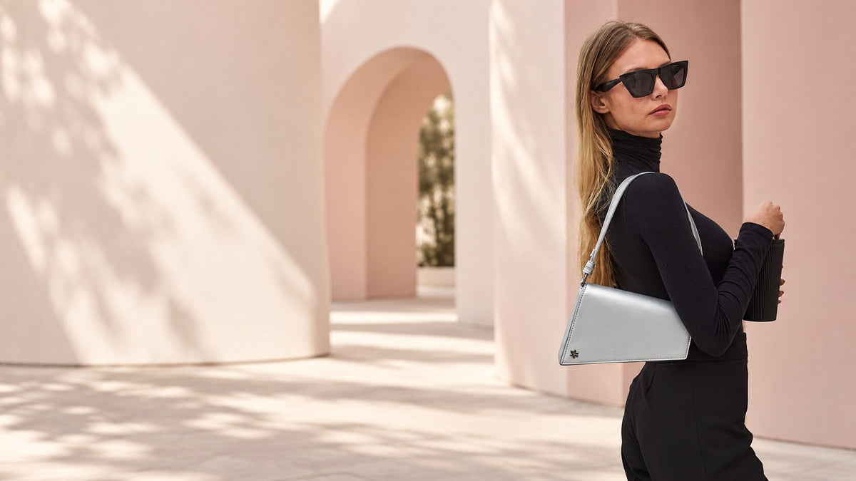Woman styling a silver Daisy Rose shoulder bag against blush architecture